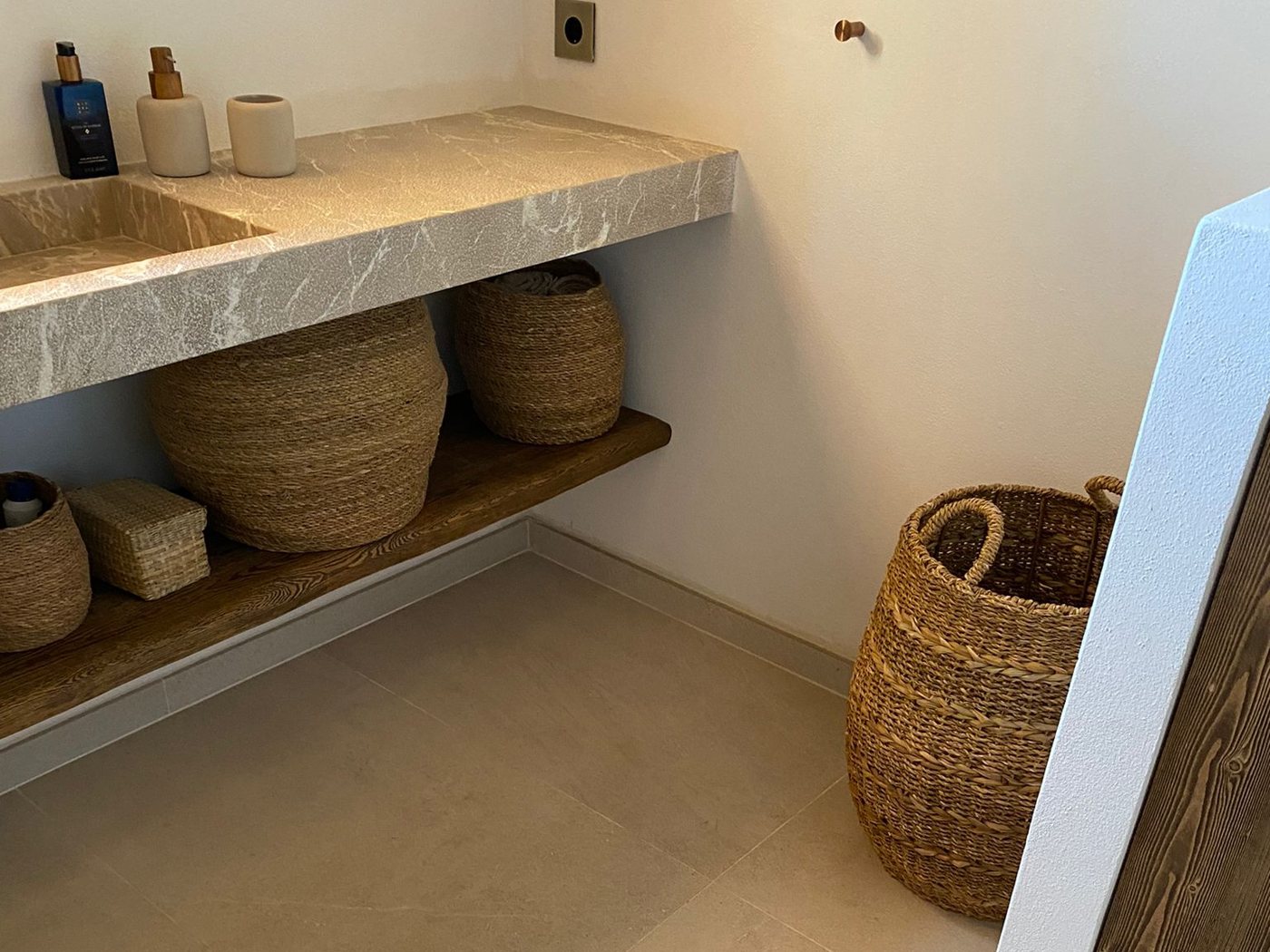Baño terminado con encimera de piedra natural, suelo de gres y cestería, obra de reforma integral